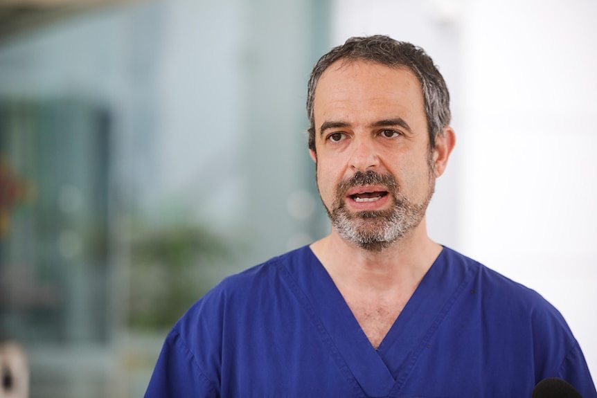 A man from mid-chest up wearing blue scrubs.