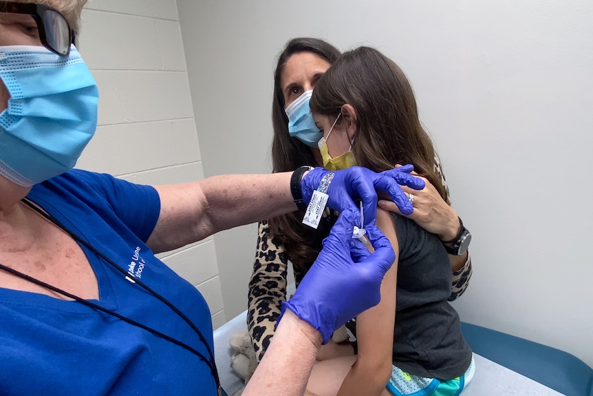A nine-year-old girl is held by her mother as she gets the second dose of the Pfizer COVID-19 vaccine during a clinical trial.