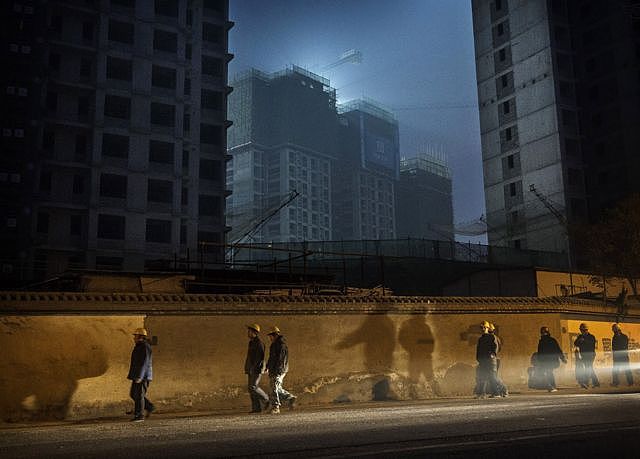 北京的工人们晚上下班后从在建的公寓楼前走过（资料图）