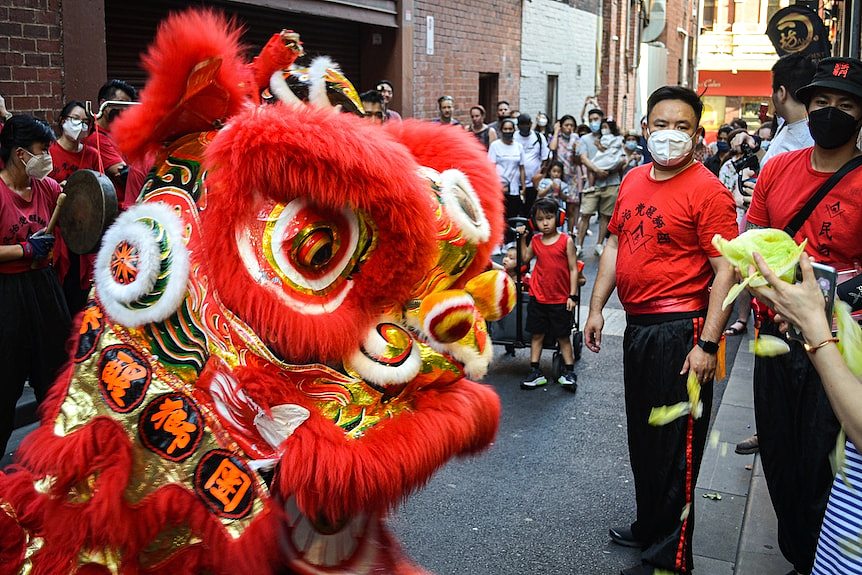 A chinese dragon on a street with a crowd behind it, wearing masks