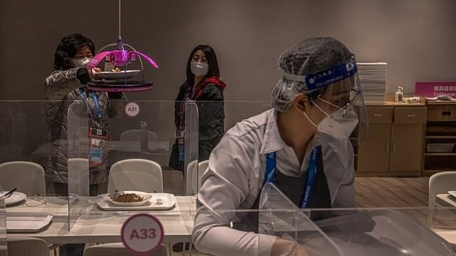 A woman picks up a dish off a food-delivering machine