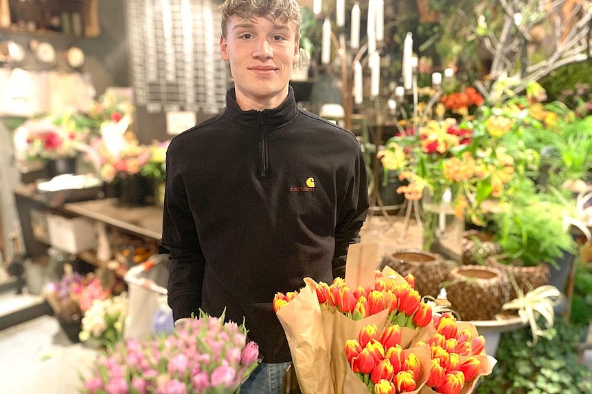 穿黑色工作服，站在花丛中的一名丹麦男青年。
