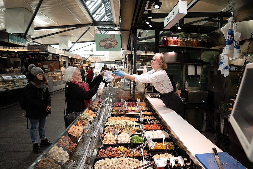 系白色围裙的年轻丹麦女子站在超市熟食柜台内。