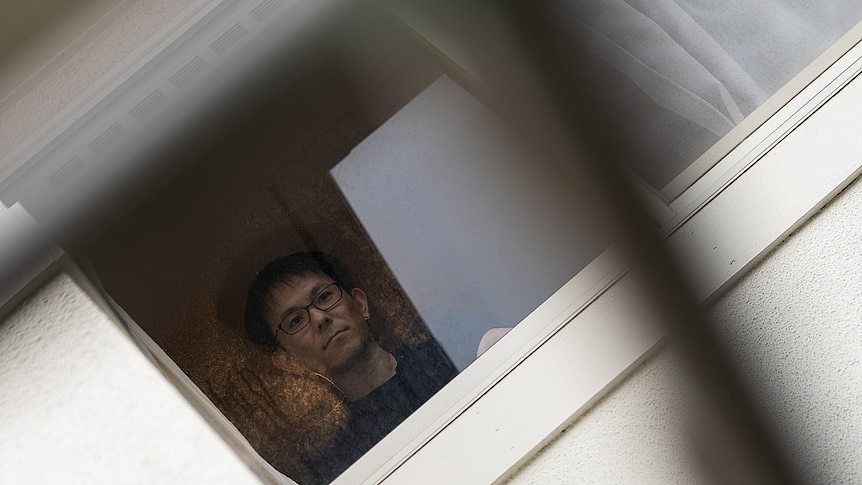 A man looks out of an upstairs window.