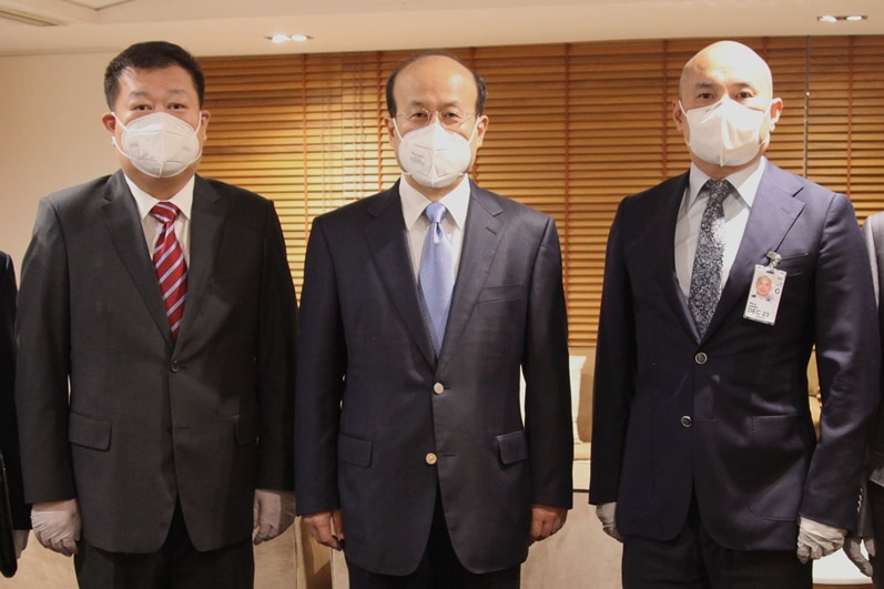 Five men wearing masks and suits pose for a photo inside an office.