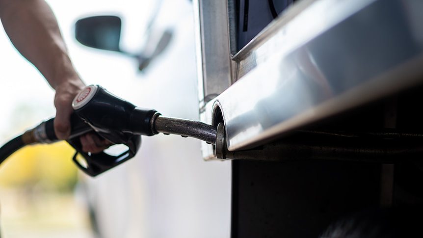 A close-up of a man's arm refuelling a white ute with a petrol bowser.