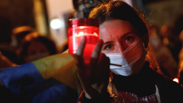 A woman holds a candle and Ukrainian flag as Ukrainian nationals living in Malta