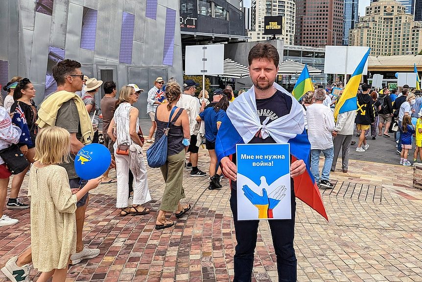 A man stands holding a sign at a street rally.