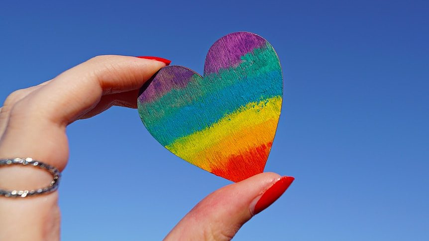 a hand holding a rainbow heart to the sky