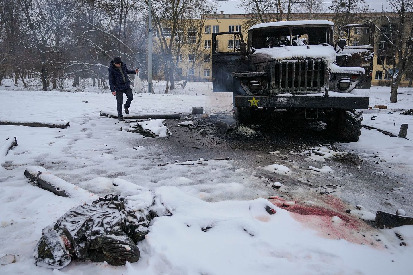 2022年2月25日，一名男子在乌克兰哈尔科夫郊区为一辆被摧毁的俄罗斯军用多管火箭发射车拍照，一名军人的尸体被雪覆盖。（AP）