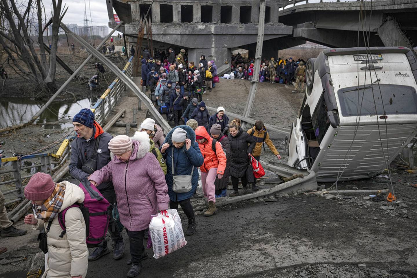 烏克蘭局勢：圖為2022年3月5日人們在逃離烏克蘭伊爾平鎮時，在一座被俄軍空襲摧毀的橋下的小路上走過。（AP）