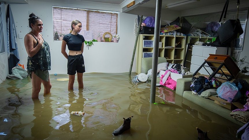 一个女人和一个女孩站在被水淹没的卧室里，脸上露出绝望的表情