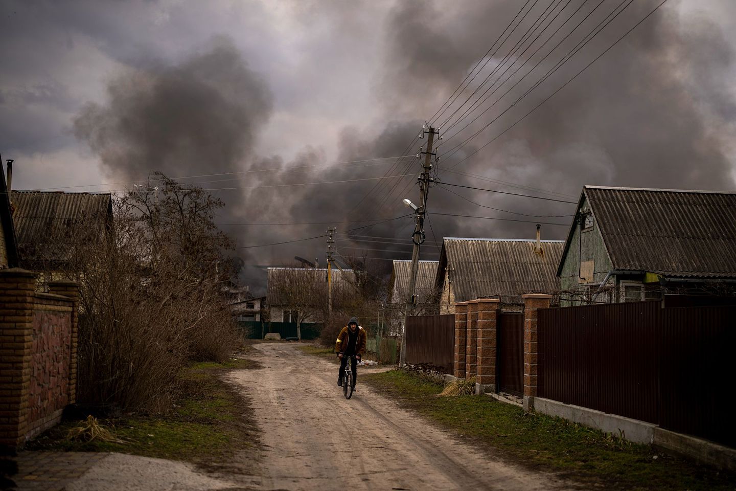 2022年3月6日，在乌克兰基辅郊区的伊尔平，一名男子骑着自行车在一家工厂和一家被轰炸后着火的商店附近穿行。（AP）