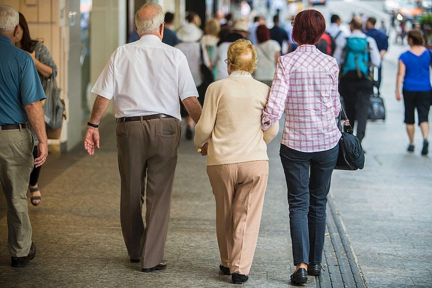 An elderly couple down a mall with the help of a younger woman.