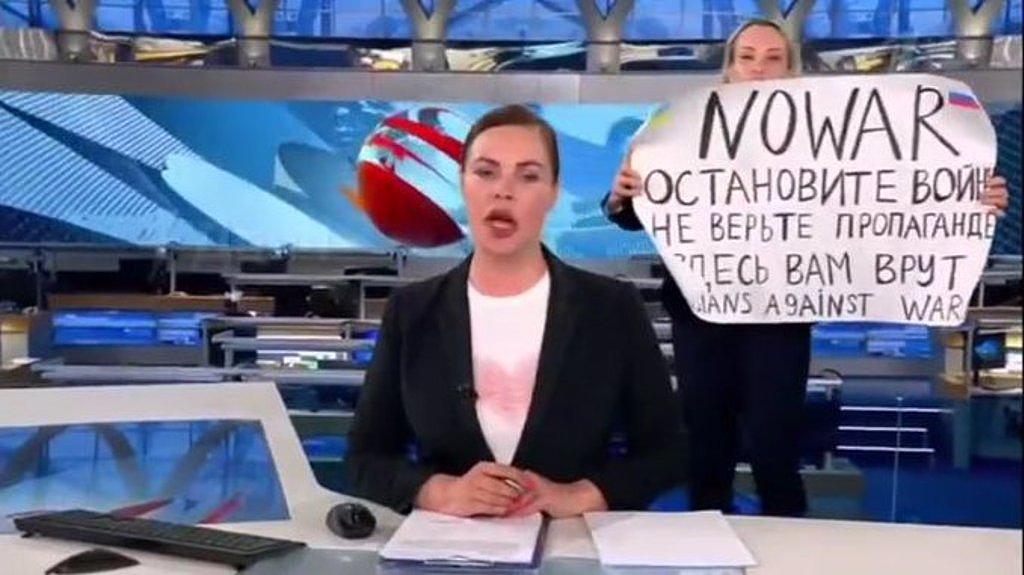 俄罗斯电视台女员工玛莉娜． 奥薇夏尼可娃在冲进直播现场站在女主播身后大喊「反对战争」，并举起一大张手写的海报，震惊了全世界。 （图／网路视频截图）