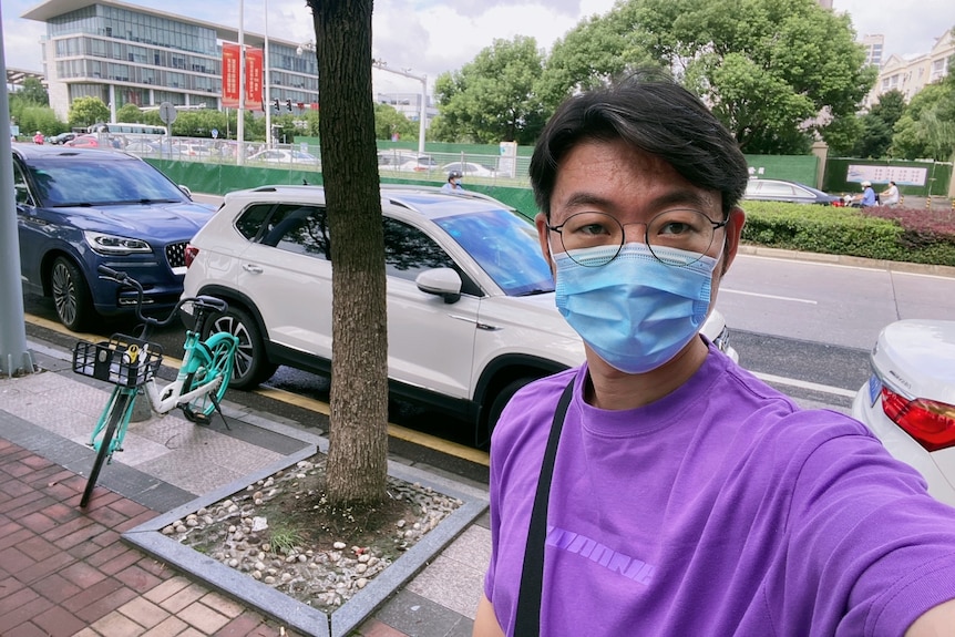 A young Chinese man in a purple t-shirt and blue face mask. 