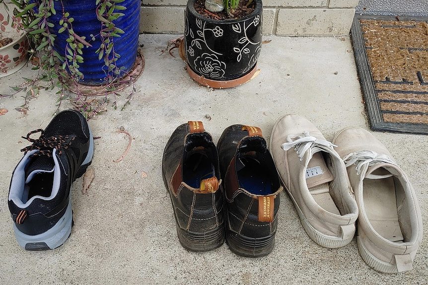 Three pairs of shoes lined up near a door mat, one shoe missing.