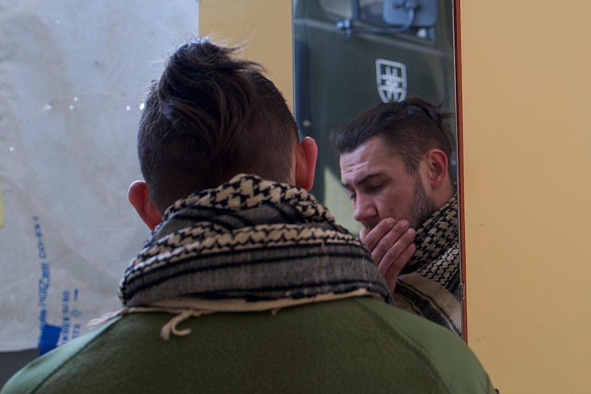 A Ukrainian soldier touches his beard looking down at a mirror