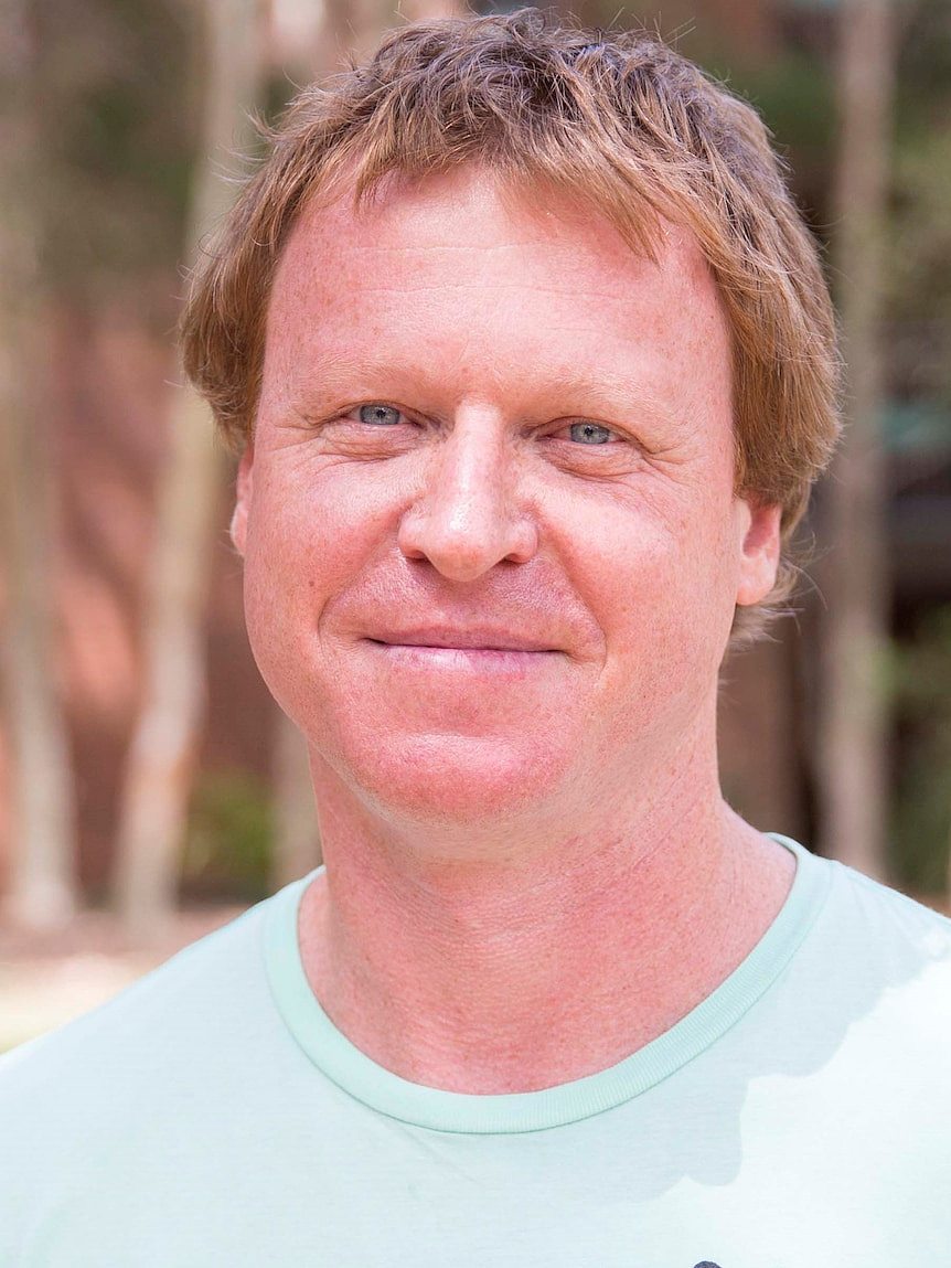 A man with red hair and a blue t-shirt looks at the camera.