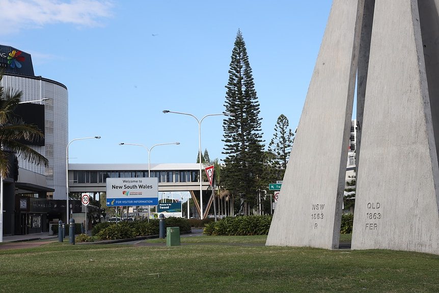 two triangular cement structures with QLD and NSW engraved in forefront, welcome to NSW sign behind