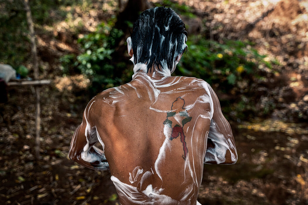 一名战士在克伦邦前哨基地的战斗间隙抽空洗了个澡，他背上是缅甸地图的文身。
