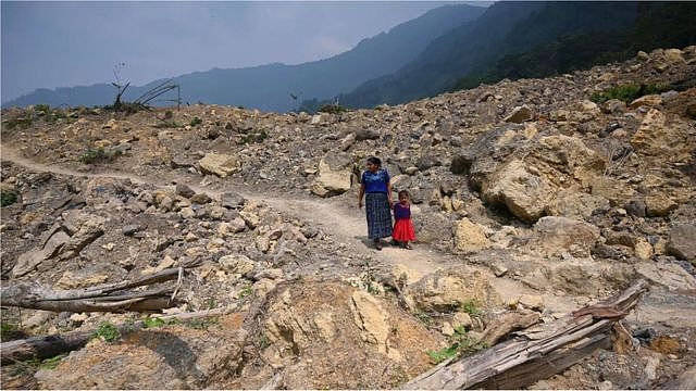 2021年瓜地马拉的克卡村在飓风带来的暴雨袭击下毁于泥石流，一位原住民女子牵着孩子走过灾害现场。