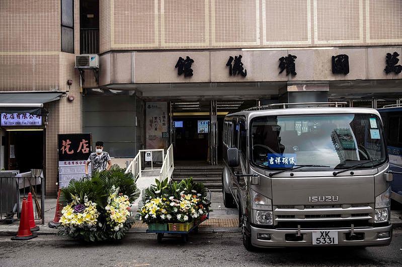 香港第五波新冠死亡患者已超过8100人，殡仪业者表示，仍需2至3个月时间，才能舒缓殓房积存遗体情况。图为一名男子（左）在香港九龙区一家殡仪馆外的手推车上搬运葬礼用花篮。（Getty Images）