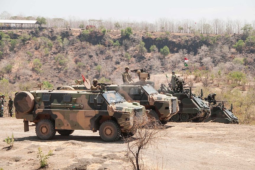 Several military personnel carriers line up in the desert.