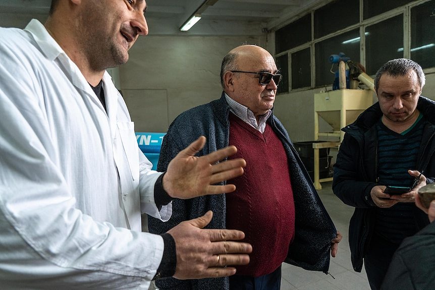 A man in a labcoat speaks to two other men inside a biofuel lab.