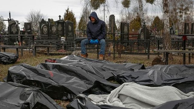 A funeral service employee sits next to bodies of civilians in Bucha