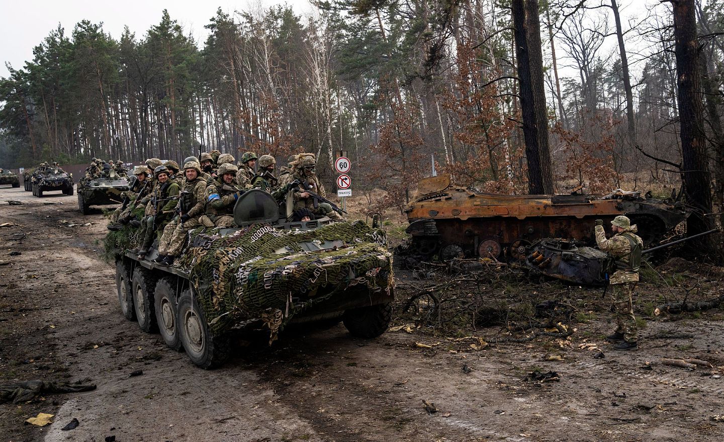 2022年3月31日，乌克兰基辅郊区，乌克兰士兵在装甲车上走过，旁边是一辆被摧毁的俄罗斯坦克。（AP）