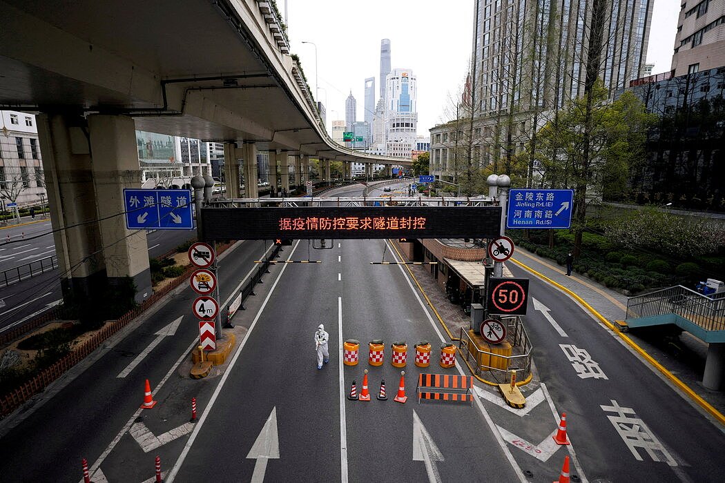 上个月因遏制病毒而被封锁的上海浦东地区，一名身穿防护服的工作人员走在马路上。
