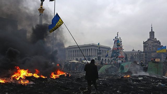 A Ukranian protester with Ukraine flag walks through rubble and burning debris after anti-government demonstrations, Independence Square, Kiev, 20 Feb 2014