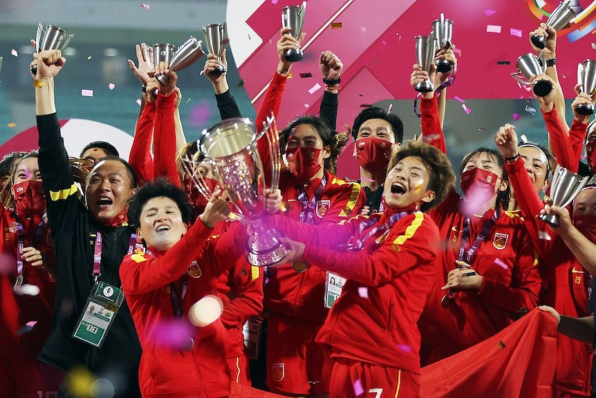 Two women footballers chase a ball. 在许多中国足球迷对国家男子足球队失去耐心的同时，女子足球队最近赢得了女子亚洲杯。