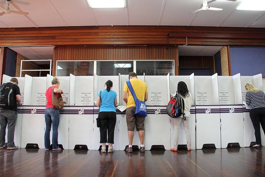 A row of people fill out forms at a polling booths during the Federal election.