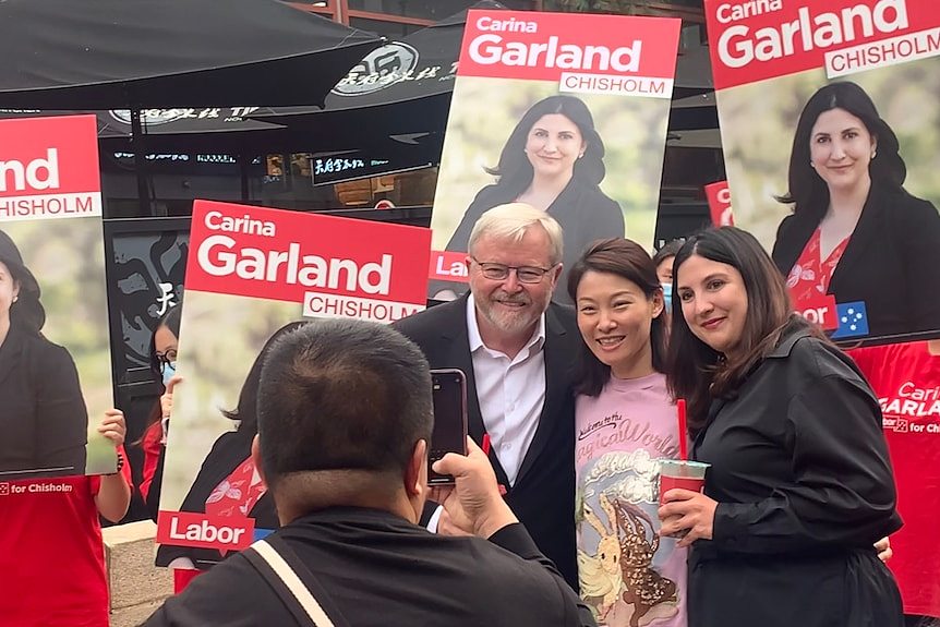 Three people pose for a photo amid red Labor campaign posters.