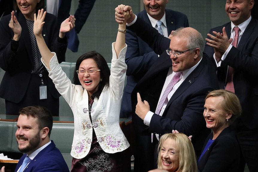 Scott Morrison holds Gladys Liu's arm in the air as he points to her with his other hand. MPs behind are smiling and clapping