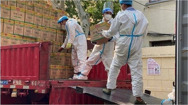 2022年4月21日，身穿防护服的人员从运往上海的卡车上卸下标有鲜味生抽的包装箱