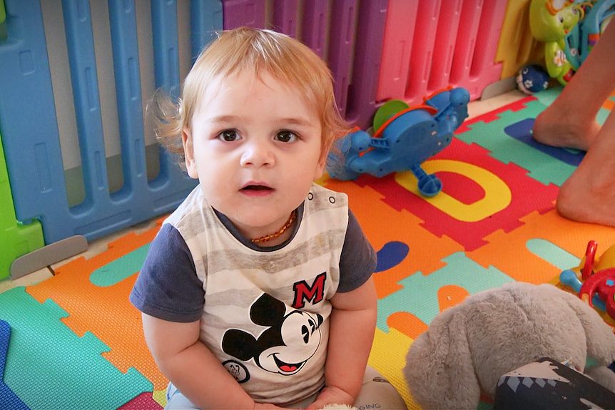 Baby boy sits on colourful floor in playpen