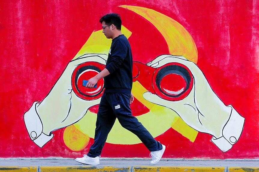 一名男子走过一面涂鸦墙，涂鸦以中国国旗为背景，前方是一名男子用望远镜看向远方