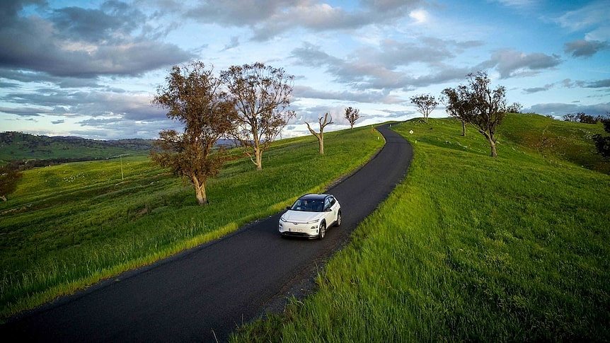 An electric car drives through green countryside.