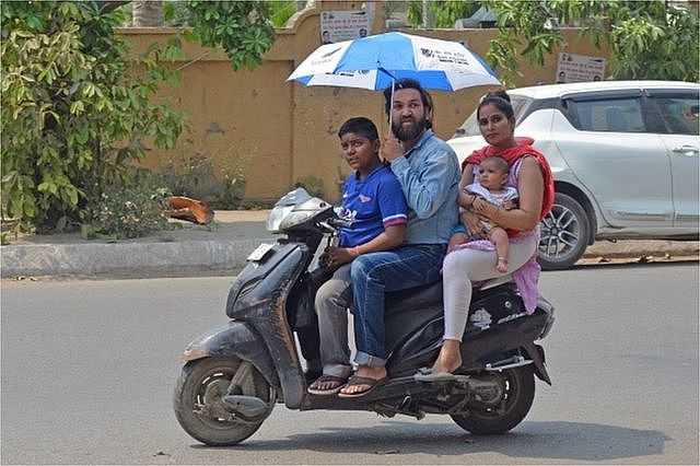 A motorist holds an umbrella while driving a scooter along a road on a hot summer day in Amritsar on May 1, 2022