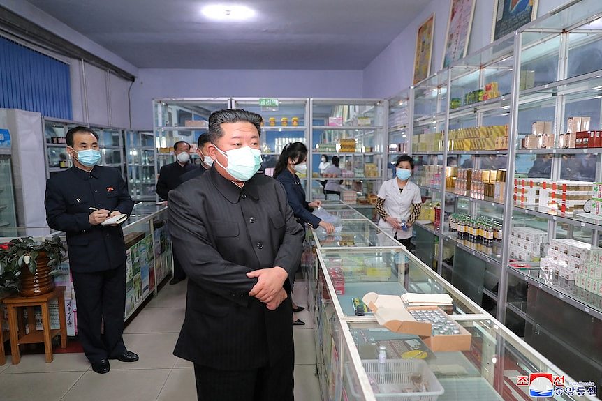 Kim Jong Un stands in front of a glass counter inside a pharmacy wearing a face mask.
