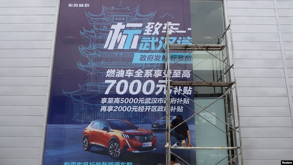 资料照：2020年8月9日，工人们在中国湖北省武汉市的一家经销店张贴了政府补贴东风标致汽车的巨幅海报。（路透社）