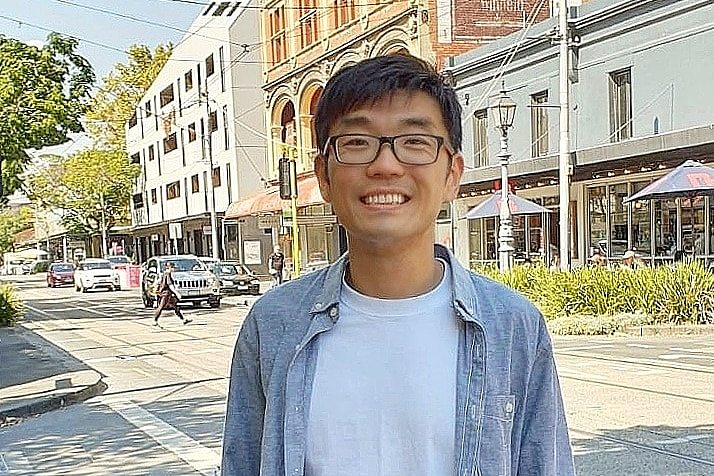 Wilfred Wang poses for a photo smiling while standing in a city street. 