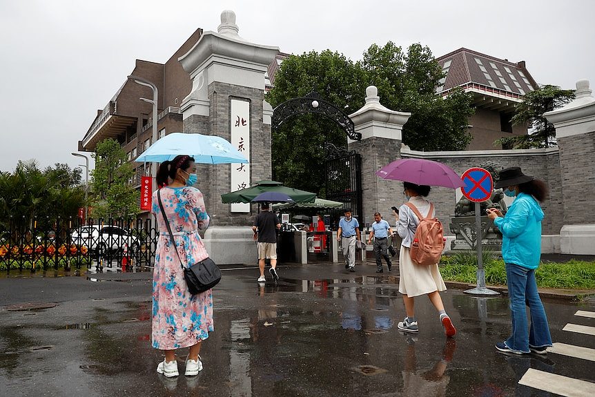 People with umbrellas walk towards the gate of a Chinese-style campus