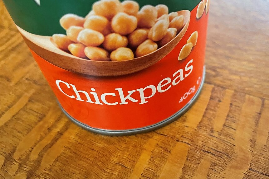 A close up of a tin of chickpeas sitting on a silky oak timber surface. 