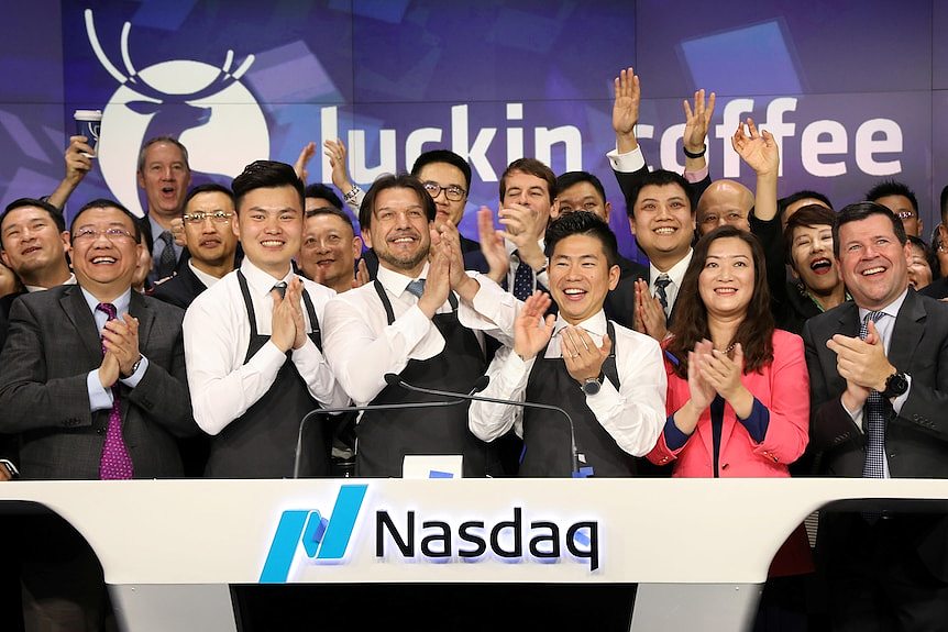 A group of Luckin employees and their CEO stands behind a desk with 