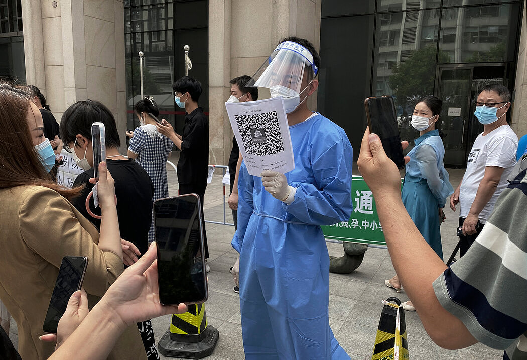 北京一名卫生工作者手持二维码，让排队等待做病毒检测的人扫描。