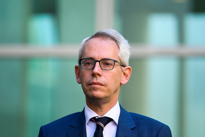 A man with glasses stands in front of parliament